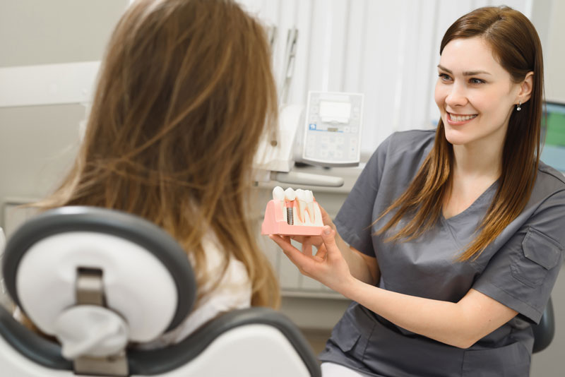 image of a dentist showing her patient a dental implant model before her facial surgery for dental implants