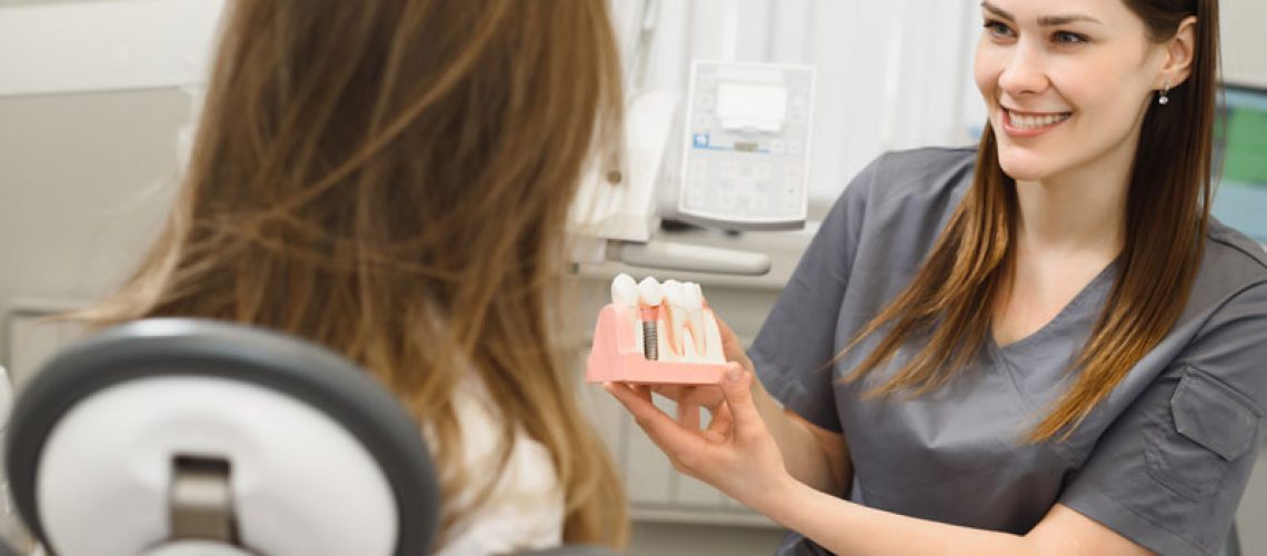 image of a dentist showing her patient a dental implant model before her facial surgery for dental implants